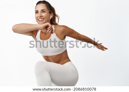 Portrait of sportswoman stretching body, exercising, doing fitness leg raise and smiling, running, standing over white background