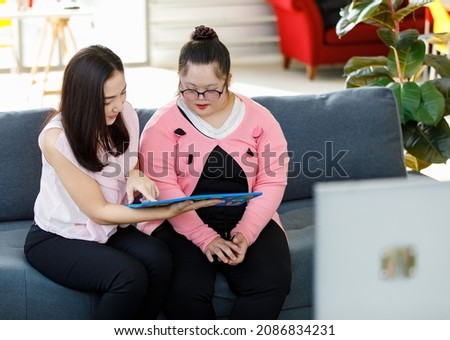 Asian lovely young mother smiling taking care and using alphabet puzzle toy teaching a girl with down syndrome daughter wearing eyeglasses on sofa in living room at home. Royalty-Free Stock Photo #2086834231