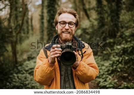 Photographer man smiling while holding camera in the woods
