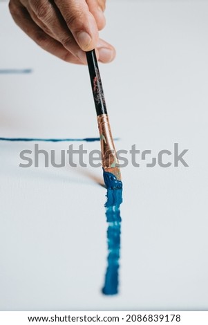 Close-up of Female senior old Artist Hand, Holding Paint Brush and Drawing Painting with blue Paint. Colorful, Emotional Oil Painting. Contemporary Painter Creating Modern Abstract Piece of Fine Art
