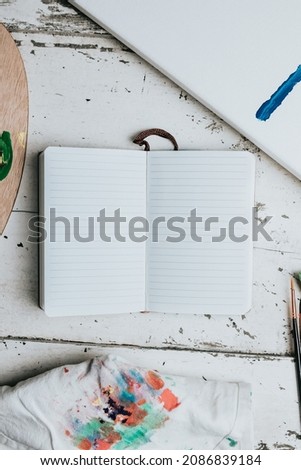 flat brushes with a notebook to take notes wit blank space and paint palette on a white wooden background. Hobby background. DIY, craft decoration for fall holidays. Flat lay, top view