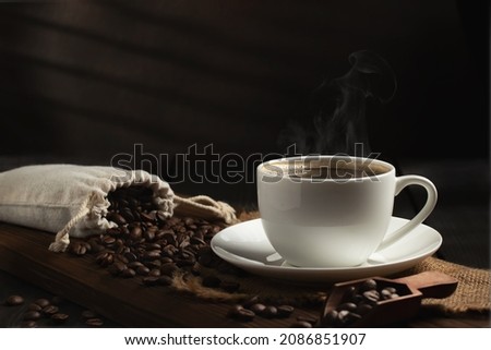 White cup of fresh hot coffee and coffee beans on wooden board on table