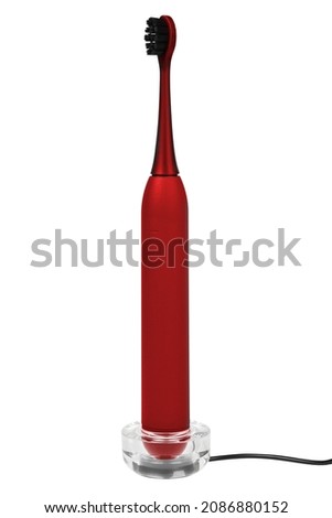 Red modern electric toothbrush gray color on a stand with a charger isolated on white background.