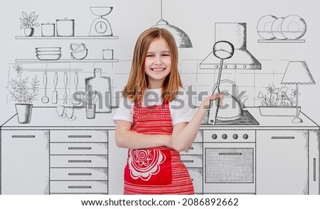 Happy little girl wearing red apron standing near wall with painted kitchen sketch