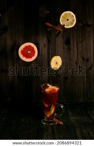 christmas mulled wine, in a transparent glass with fruit on a dark wooden background surrounded by flying spices and fruits