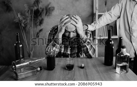 A drunken person's family has a problem with alcohol. Upset woman put her hand on the man's shoulder. concept of support for alcoholics and addiction treatment. Copy space. Black and white photo