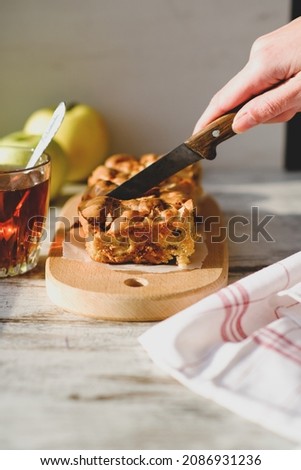 Culinary food template. Homemade Charlotte apple pie on a wooden plate with tea and apples in the background. A woman’s hand with a knife is cutting the pie. Sweet organic vegan plant-based bakery. 
