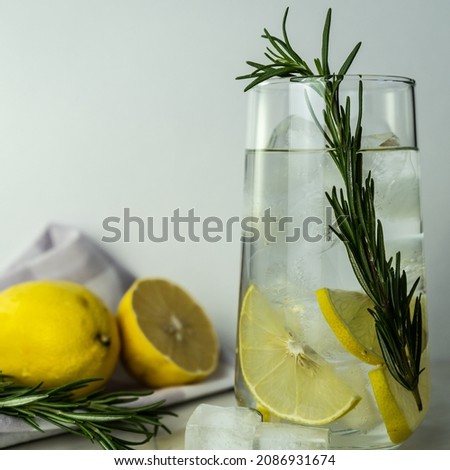 a glass of water with lemon and a sprig of rosemary with ice. A glass of water with ice. Gin,lemon, rosemary fizz, cocktail with honey and fresh herbs on a white background. Selective focus.