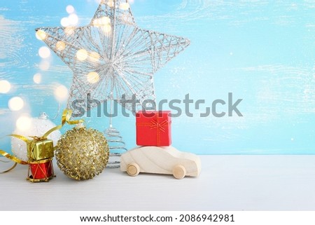 Image of christmas decorations and wooden car with present box in front of pastel blue background