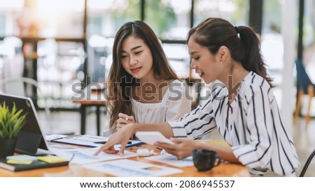 Two young Asian businesswoman discuss investment project working and planning strategy. Business people talking together with laptop computer at office. Royalty-Free Stock Photo #2086945537