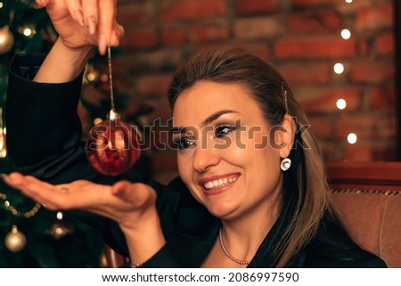 Portrait of a beautiful young stylish woman in a black suit holding a brown ball in her hands.Dark loft interior design.Christmas tree in the background.New Year and Christmas concept.