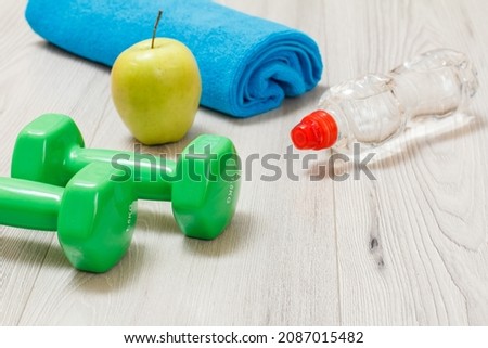 Green dumbbells for fitness, a bottle of water, an apple and a towel on the background.