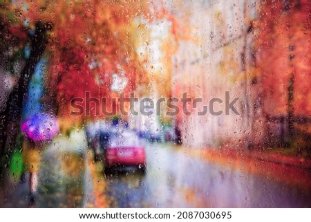 View of a blurred rainy autumn city   street through glass covered with rain drops. Focus on drops