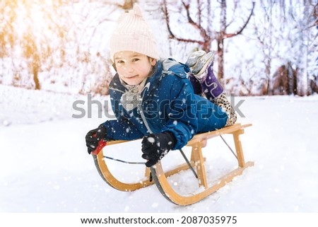 Two children ride on wooden retro sled on sunny winter day. Active winter outdoors games. Winter activities for kids. Children playing with snow in park. 