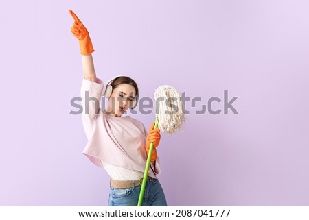 Young woman with floor mop listening to music on color background