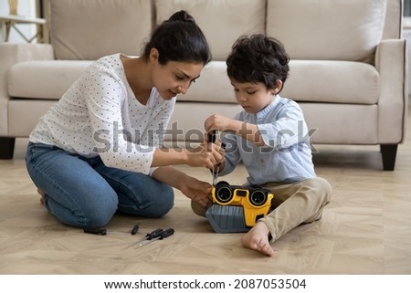 Happy young Indian mother helping adorable small kid son fixing toy car with screwdriver, playing together at home. Smiling mum teaching little child repairing, developing motility skills Royalty-Free Stock Photo #2087053504