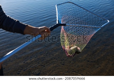 Fisherman holding fishing net with catch at riverside, closeup