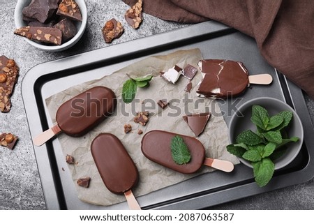 Flat lay composition with glazed ice cream bars, fresh mint and chocolate on grey table