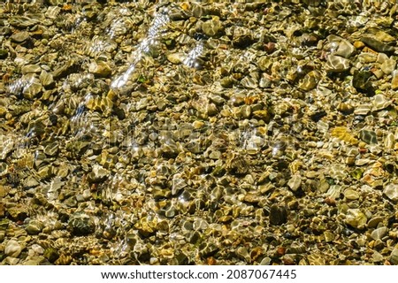 Pebbles at the bottom of a mountainous, transparent river. The sun's rays are reflected off the water.