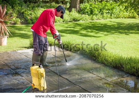 Jet washing a patio. Woman high pressure washing, power washing or cleaning a garden terrace, UK