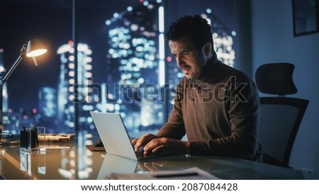 Portrait of Thoughtful Successful Businessman Working on Laptop Computer in His Big City Office at Night. Charismatic Digital Entrepreneur does Data Analysis for e-Commerce Strategy.