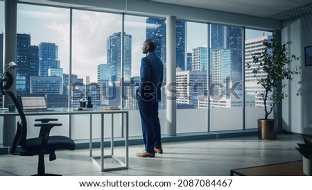 Thoughtful African-American Businessman in a Perfect Tailored Suit Standing in His Office Looking out of the Window on Big City. Successful CEO Planning His Investment Strategy for e-Commerce Startup Royalty-Free Stock Photo #2087084467