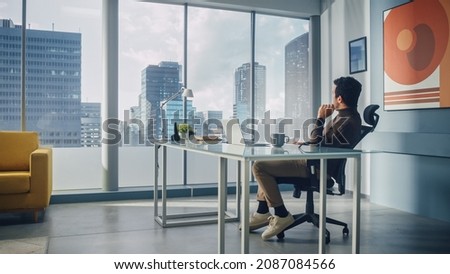 Portrait of Charismatic Arab Businessman Sitting at His Desk Working on Laptop Computer in Big City Office. Successful Digital Entrepreneur Doing Data Analysis for e-Commerce Startup. Royalty-Free Stock Photo #2087084566