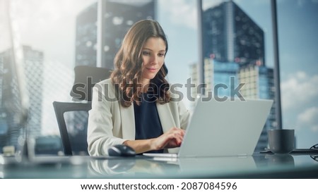 Portrait of Successful Young Businesswoman Sitting at Her Desk Working on Laptop Computer in Big City Office. Confident Professional CEO Managing Environmental, Social and Corporate Governance Royalty-Free Stock Photo #2087084596