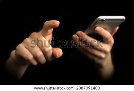 Person uses mobile phone with index finger. Hand with modern smartphone on a black background, communication and techonology concept 