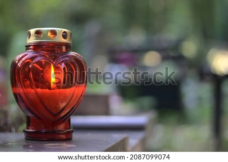 A red heart - shaped candle (snitch) on a tombstone in a cemetery during the day. All Saints' Day, copy space. Royalty-Free Stock Photo #2087099074