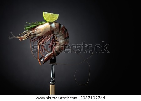 Fresh tiger prawn with rosemary and lime slice on a black background. Copy space.