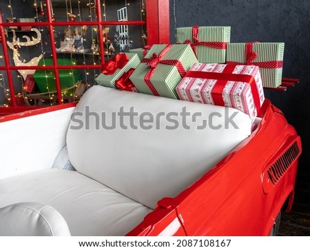 Photo of a red cabriolet car with multi-colored boxes with gifts for the New Year against a background of glowing lights. Christmas.