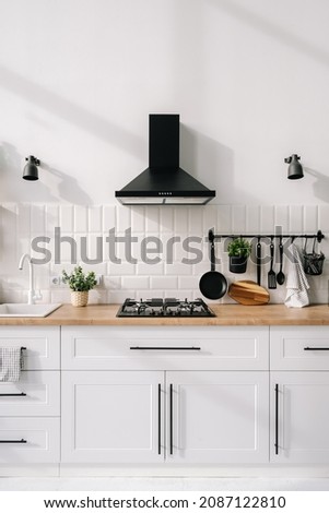 Modern kitchen interior design in white tones with a hob, sink, hood and appliances. Wooden furniture concept. Luxury apartment for rent. New comfortable home Royalty-Free Stock Photo #2087122810