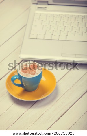 Cup of coffee with heart shape and notebook on wooden table.