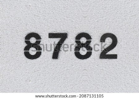 Black Number 8782 on the white wall. Spray paint. Number eight thousand seven hundred and eighty two.