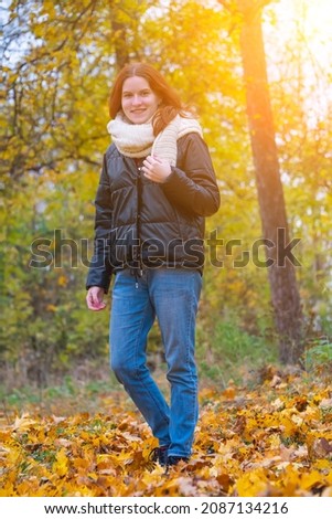 a portrait of a red - haired smiling girl in a jacket and scarf with her hair loose in full growth walks in the park . against the background of autumn nature, the concept of human emotion.