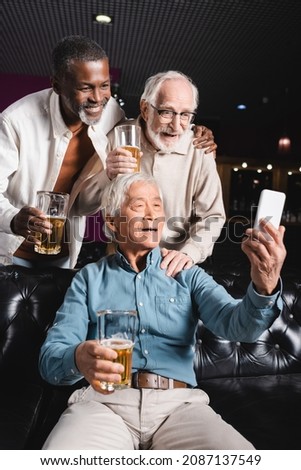 senior asian man sitting on couch and taking selfie with senior friends in beer pub