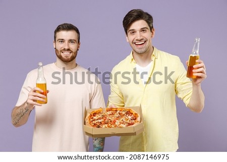 Two cool young men friends together 20s in casual t-shirt tattoo translate fun eat italian pizza in cardboard flatbox drink beer isolated on purple background studio portrait People lifestyle concept