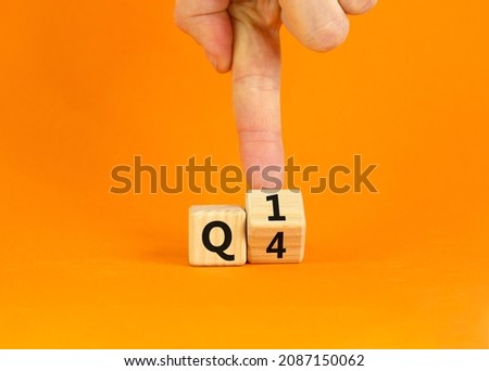 From 4th to 1st quarter symbol. Businessman turns a wooden cube and changes words 'Q4' to 'Q1'. Beautiful orange table, orange background. Business, happy 1st quarter Q1 concept, copy space.