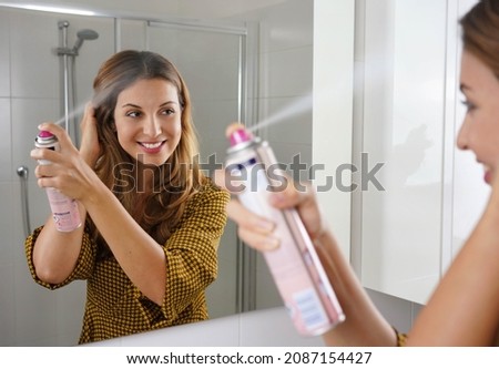 Fast and easy way to covering grey hair with instant spray dye. Young woman applying dry shampoo on her hair before going out. Royalty-Free Stock Photo #2087154427