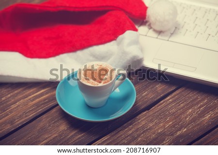 Cup of coffee with heart shape, laptop and christmas hat.