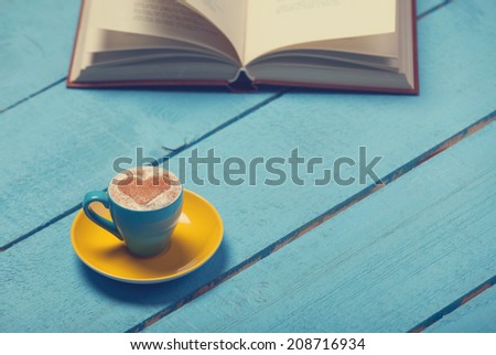 Cup of coffee with book on blue wooden table.
