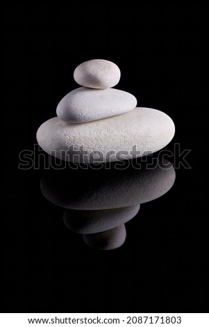 Composition of three white stones, photographed against a black background with reflection. Still life, can be used for decorative purposes.