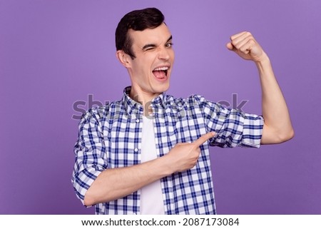 Photo of young excited guy indicate finger arm muscles wink eye body builder isolated over violet color background