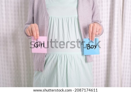 close-up of pregnant woman holding pink and blue paper note choose and promote boy or girl. woman expecting baby, family and parenting concept