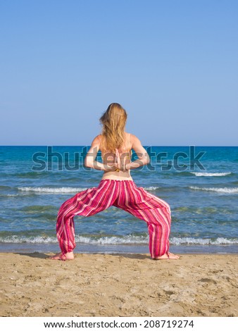 Beautiful young woman practicing yoga on the beach