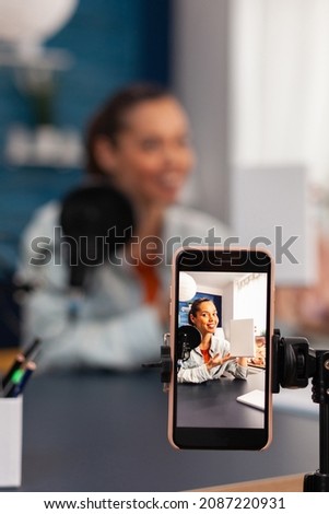 Closeup of smartphone recording white box review. Mobile phone filming smiling influencer doing product recommendation. Social media online podcast in home recording studio with microphone.
