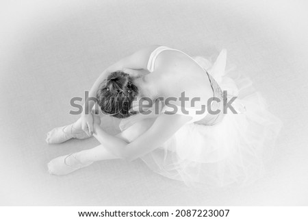 The ballerina is sitting on the floor with her head bowed and her back bare. The concept of dance art.