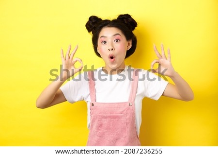 Excited beauty girl with bright makeup and summer clothes, showing okay signs and say wow, praise good promo deal, approve advertisement, yellow background