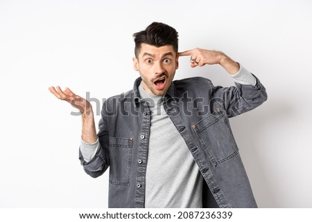 Are you crazy. Angry man scolding person for stupid actions, pointing at head temple and raising hand confused, complaining while standing on white background Royalty-Free Stock Photo #2087236339